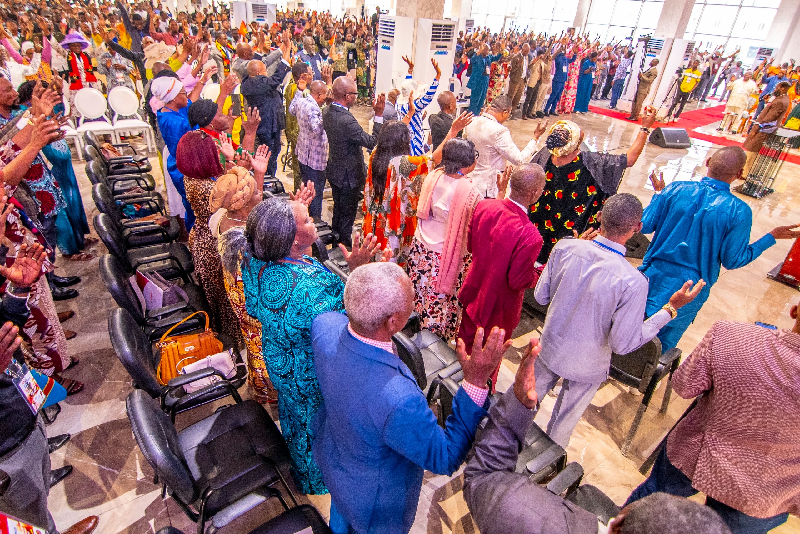 A conference hall in the DRC on its feet, hands raised in worship.