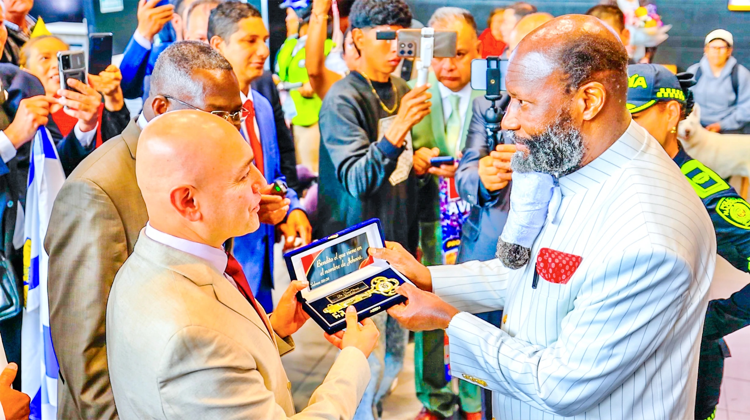 The Prophet receiving a ceremonial golden key in a presentation case, surrounded by people filming.